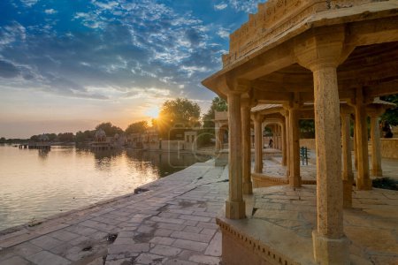 Foto de Chhatris and shrines of hindu Gods and goddesses at Gadisar lake, Jaisalmer, Rajasthan, India. Indo-Islamic architecture , sun set and colorful clouds in the sky with view of the Gadisar lake. - Imagen libre de derechos