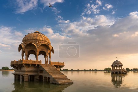 Foto de Chhatris and shrines of hindu Gods and goddesses at Gadisar lake, Jaisalmer, Rajasthan, India with reflection on water. Indo-Islamic architecture , sun set and colorful clouds with Gadisar lake. - Imagen libre de derechos
