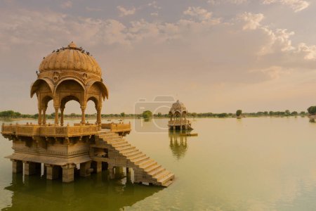 Foto de Chhatris and shrines of hindu Gods and goddesses at Gadisar lake, Jaisalmer, Rajasthan, India with reflection on water. Indo-Islamic architecture , sun set and colorful clouds with Gadisar lake. - Imagen libre de derechos