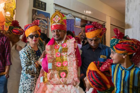 Foto de Jodhpur, Rajastán, India - 19.10.2019: Novio sonriendo, llevando guirnalda de dinero para Baraat o procesión para llegar al lugar de la boda con familiares y amigos. Ceremonia de matrimonio Sindhi en hotel. - Imagen libre de derechos