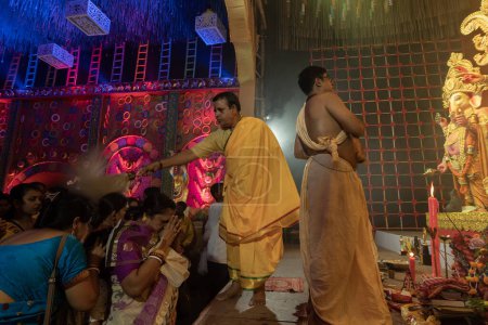 Téléchargez les photos : Howrah, Bengale occidental, Inde - 3 octobre 2022 : Prêtre hindou bénissant les dévots priant avec chamor, mouche fouetter fan à l'intérieur de Durga Puja pandal. Ashtami puja aarati la nuit. Le plus grand foetus de l'hindouisme. - en image libre de droit