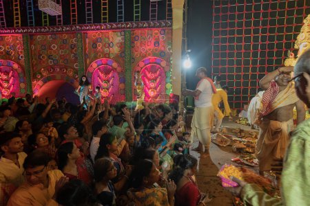 Photo for Howrah,West Bengal,India- 3rd October, 2022 : Hindu purohit spraying Holy water, called shantir jol, upon devotees worshipping Goddess Durga, inside decorated Durga Puja Pandal at night. Durga puja. - Royalty Free Image