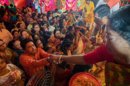 Photo for Howrah,West Bengal,India- 4th October, 2022 : Hindu woman distributing flower petals for pushpanjali to devotees, for praying and worshipping Goddess Durga, inside decorated Durga Puja Pandal. - Royalty Free Image