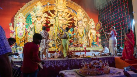 Photo for Howrah, West Bengal, India - 5th October, 2022 : Hindu Purohits offering Vog, holy sweet food to Goddess Durga while Dhaakis playing dhaaks, inside Durga puja pandal covered with holy smoke. - Royalty Free Image