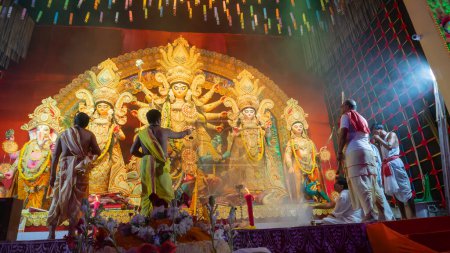 Foto de Howrah, Bengala Occidental, India - 5 de octubre de 2022: Purohits hindúes ofrecen Vog, comida dulce sagrada para la Diosa Durga mientras la adoran dentro de Durga puja pandal cubierta de humo sagrado. - Imagen libre de derechos
