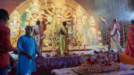Téléchargez les photos : Howrah, Bengale Occidental, Inde - 5 octobre 2022 : Les Dhaakis jouent aux dhaaks pour adorer la Déesse Durga, tandis que la Déesse est offerte Vog, nourriture sainte et sucrée. Un rituel sacré Durga Puja à l'intérieur du pandal puja. - en image libre de droit