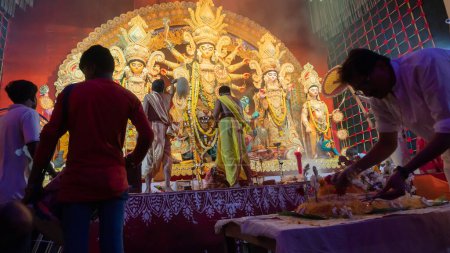 Téléchargez les photos : Howrah, Bengale Occidental, Inde - 5 Octobre, 2022 : Purohits hindous offrant Vog, nourriture douce sainte à la déesse Durga tandis que les Dhaakis jouent aux dhaaks, à l'intérieur de Durga puja pandal couvert de fumée sainte. - en image libre de droit