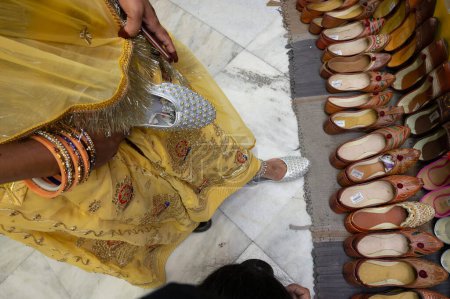 Beautiful Indian Rajasthani woman trying out her foot for fitting of colorful Rajsathani ladies shoes at shoe store at famous Sardar Market and Ghanta ghar Clock tower in Jodhpur, Rajasthan, India.