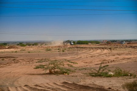 Industrietraktor durch Sand auf dem Boden in der Wüste Thar, Rajasthan, Indien. Staub fliegt durch die Luft.