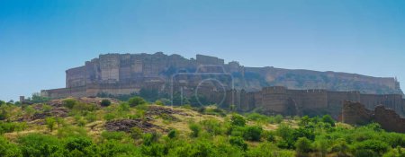 Panoramic view of Mehrangarh fort from Rao Jodha desert rock park, Jodhpur, India. Green vegetation in the foreground and Mehrangarh fort in the background, with rocky landscape of the desert park.