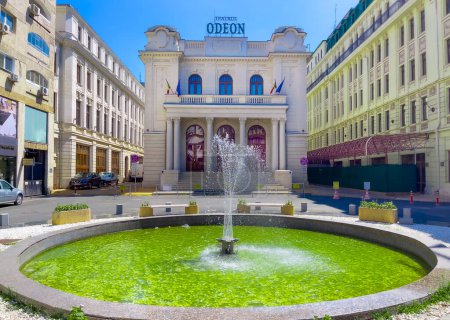 Foto de Bucarest, Rumania, Europa - 15 de julio de 2023: Vista frontal del famoso edificio cultural de las artes Odeon Theatre City y la fuente verde iluminada en un día soleado - Imagen libre de derechos