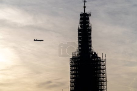 Photo for A plane flying very close to a building under construction. Sun rising in the background and backlighting the building. - Royalty Free Image