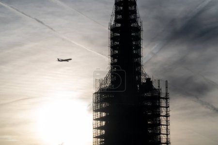 Photo for A plane flying very close to a building under construction. Sun rising in the background and backlighting the building. - Royalty Free Image