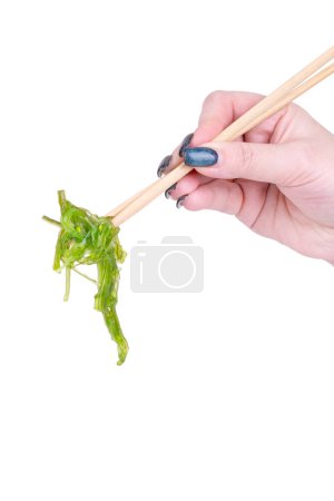 Téléchargez les photos : Main de femme tenant une salade de chuka aux algues avec des baguettes chinoises sur fond blanc - en image libre de droit