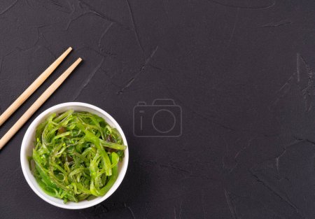 Téléchargez les photos : Salade d'algues fraîches chuka dans une assiette avec baguettes sur fond sombre - en image libre de droit
