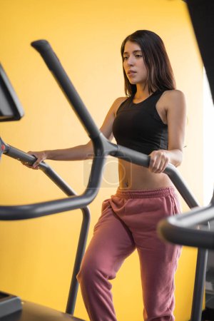 Foto de Uso de la máquina en el gimnasio para el ejercicio, mujer latina joven en ropa deportiva, estilo de vida saludable y bienestar, aparatos para el deporte - Imagen libre de derechos