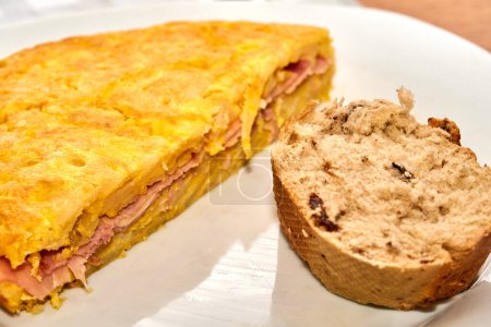 Téléchargez les photos : Omelette espagnole avec jambon et une tranche de pain complet aux noix sur une assiette. Concentration sélective. - en image libre de droit