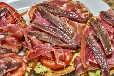 Photo for Suggestive Iberian ham toasts, tomato slices and fresh avocado. - Royalty Free Image