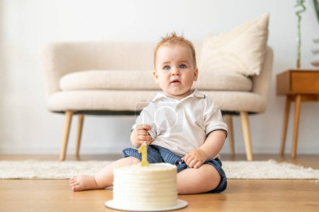 Ein Baby, das auf dem Boden neben einer Torte sitzt und die Leckereien neugierig und aufgeregt betrachtet.