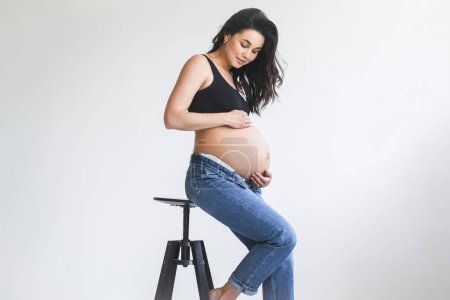 A pregnant woman is shown sitting on a stool in this photo.