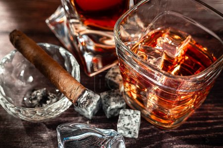 Foto de A gA glass of scotch whiskey with ice and a cigar on a wooden table close-up. Food photo. - Imagen libre de derechos