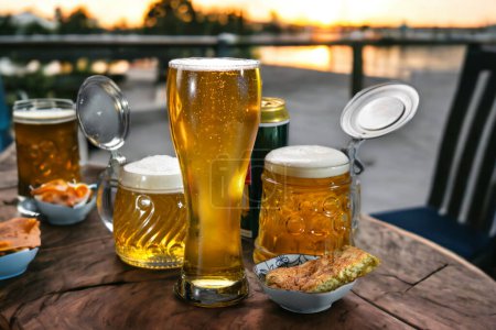 Téléchargez les photos : La bière dans un verre à bière et dans des tasses à bière se tient sur une table sur le balcon dans le contexte de la nature. Bière. - en image libre de droit