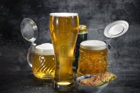 Téléchargez les photos : La bière dans un verre à bière et dans des tasses à bière se dresse sur un fond sombre. Bière. - en image libre de droit