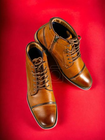 A pair of premium calfskin boots on a red background. Vertical shot. Men's shoe ideas.
