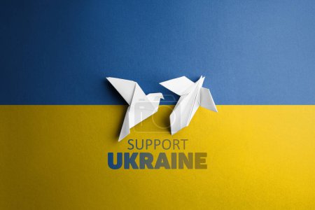 zwei weiße Papiertauben in der Mitte auf dem Hintergrund mit Wörtern unterstützen die Ukraine, mit blaugelber Farbe. Symbol der Freiheit