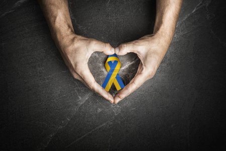 Foto de Male hands with yellow and blue ribbon on marble background. concept needs help and support, truth will win - Imagen libre de derechos