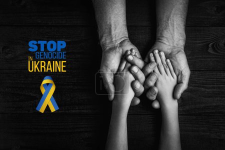 Foto de Manos masculinas sostienen a los niños sobre un fondo oscuro con palabras detener el genocidio en Ucrania con cinta amarilla y azul. color blanco y negro. concepto necesita ayuda y apoyo, la verdad va a ganar - Imagen libre de derechos