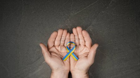 Foto de Male hand with yellow and blue ribbon on marble background. concept needs help and support, truth will win - Imagen libre de derechos