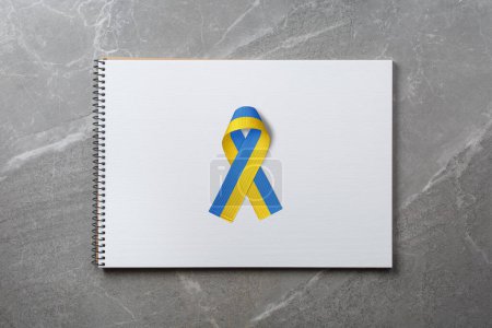 Foto de Cinta azul amarillo ucraniano en el centro del cuaderno en la mesa de mármol. concepto necesita ayuda y apoyo, la verdad va a ganar - Imagen libre de derechos