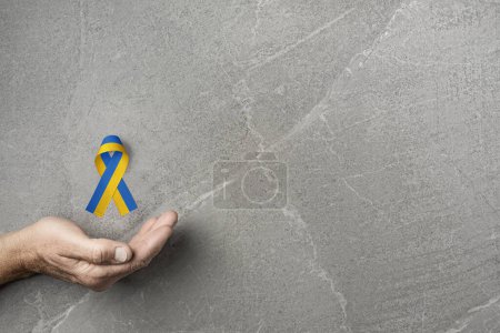 Foto de Male hand with yellow and blue ribbon on marble background. concept needs help and support, truth will win - Imagen libre de derechos