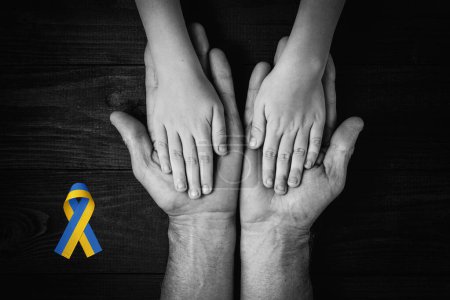 Foto de Male hands hold childrens on dark wooden background with yellow and blue ribbon. black and white color. concept needs help and support, truth will win - Imagen libre de derechos