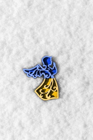 Foto de Yellow blue wooden angel on white snow as a symbol of support for ukraine in winter. concept needs help and support, truth will win - Imagen libre de derechos
