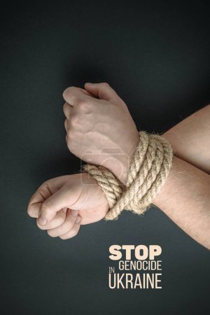 male hands tied with rope on dark green background, violence and kidnapping. with words stop genocide in ukraine. concept needs help and support, truth will win
