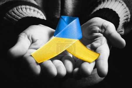 Foto de La mano de Childs sostiene la cinta ucraniana azul y amarilla sobre fondo oscuro. color blanco y negro. concepto necesita ayuda y apoyo, la verdad va a ganar - Imagen libre de derechos