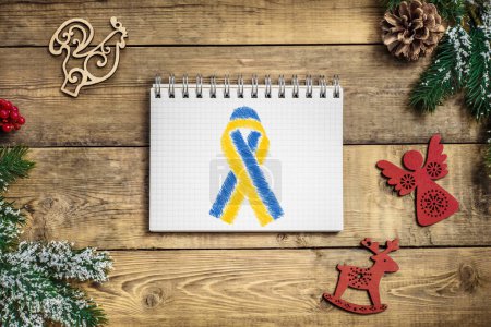 Foto de Cinta azul y amarilla ucraniana en medio de un cuaderno sobre un fondo navideño de madera. concepto necesita ayuda y apoyo, la verdad va a ganar - Imagen libre de derechos