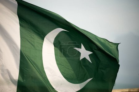 The national flag of Pakistan flying in the blue sky with clouds