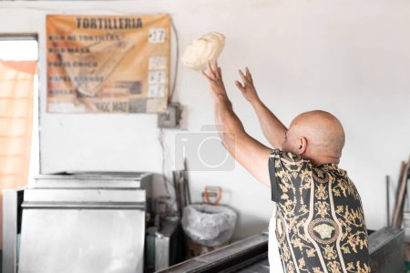 An adult tortilla maker is ready to throw a corn dough ball into the kneading machine in Mexico