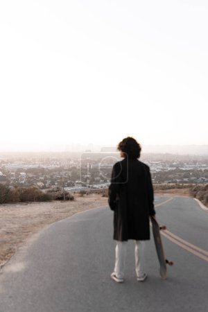 Téléchargez les photos : A view of Los Angeles cityscape with a blurred young man looking holding his skate in Baldwin Hills during the sunset, Los Angeles. Concept of skate lifestyle - en image libre de droit