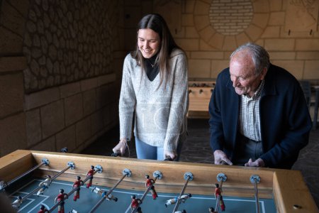 Photo for A granddaugther and his grandfather are playing table football game and having fun together. Concept of family fun time - Royalty Free Image