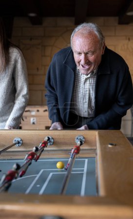Téléchargez les photos : Un grand-père et son grand-père jouent au baby-foot et s'amusent ensemble. Concept de plaisir en famille - en image libre de droit