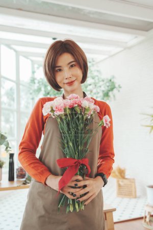 Photo for Portrait of a charming Asian Korean Woman florist holding a bouquet of carnation flowers in hands at floral shop. Small business, Entrepreneur - Royalty Free Image