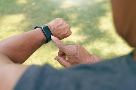 Nahaufnahme asiatischer Seniorenhände, die im Naturpark seinen Herzschlag mit einer Smartwatch überprüfen. Ältere Männer kontrollieren nach dem Joggen den Puls. Fitness-Tracker