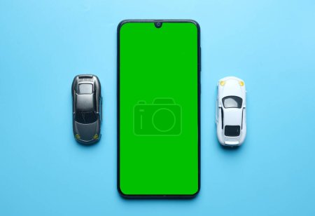 Téléchargez les photos : Flatlay picture of smartphone green chroma key with two diorama cars miniature on blue background. Online car dealing concept. - en image libre de droit