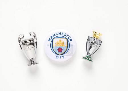 Foto de 'Kuala Lumpur, Malasia - Circa marzo, 2023: Una imagen plana del logotipo de la insignia del Manchester City con réplica de la Liga de Campeones de la UEFA y la miniatura del trofeo EPL sobre fondo blanco." - Imagen libre de derechos