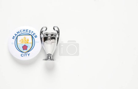 Foto de 'Kuala Lumpur, Malasia - Circa marzo, 2023: Una imagen plana del logotipo de la insignia del Manchester City con réplica de la miniatura del trofeo de la Liga de Campeones de la UEFA sobre fondo blanco." - Imagen libre de derechos