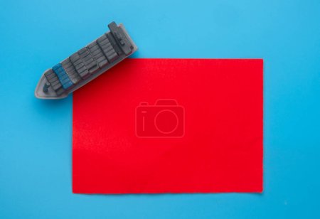 Flatlay picture of vessel miniature on red paper and blue background. Shipment crisis concept.